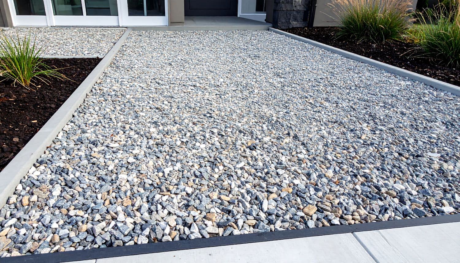A crushed stone driveway held between concrete edges, with planting either side