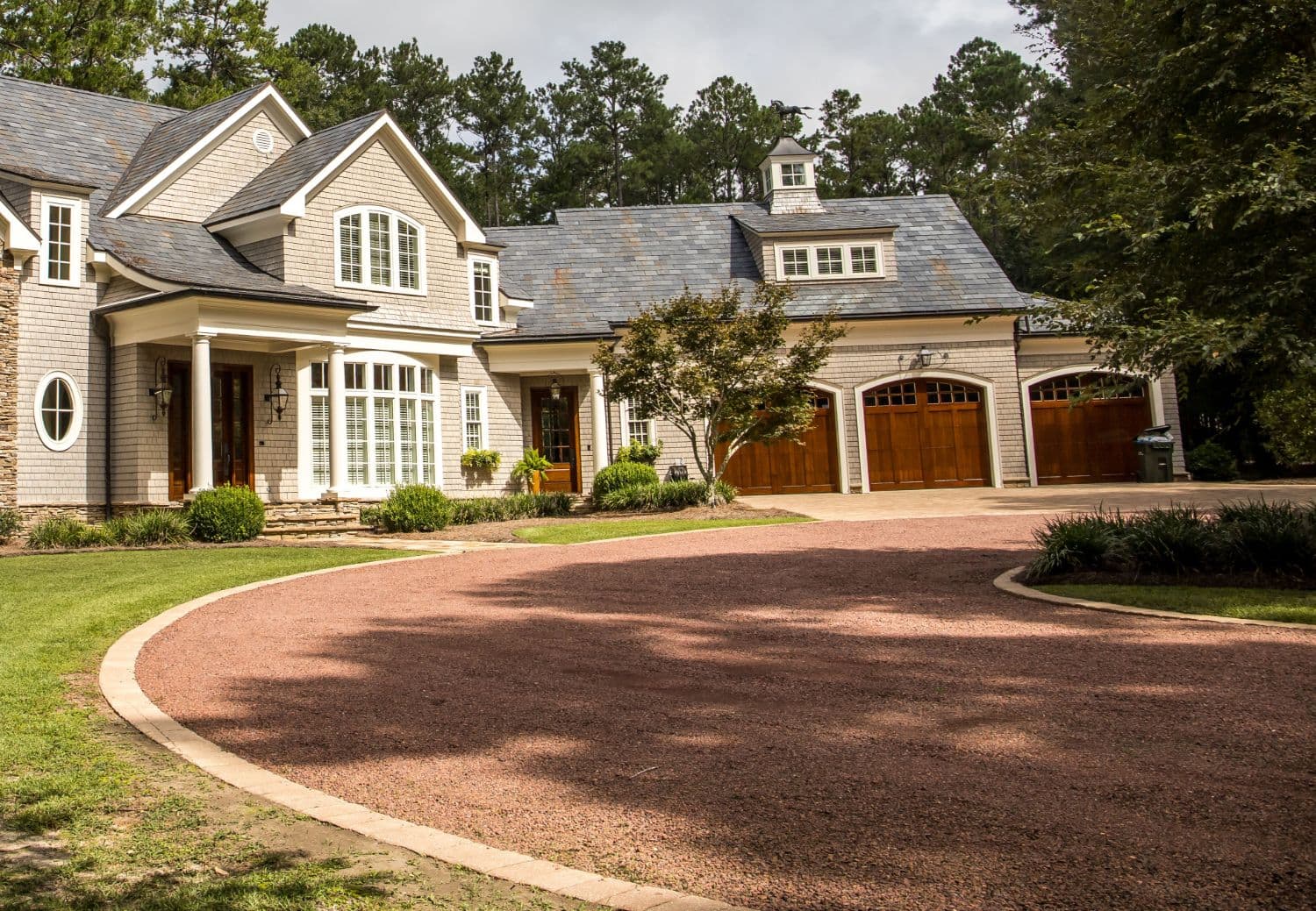 A wide crushed stone driveway curving up to a large shingled house
