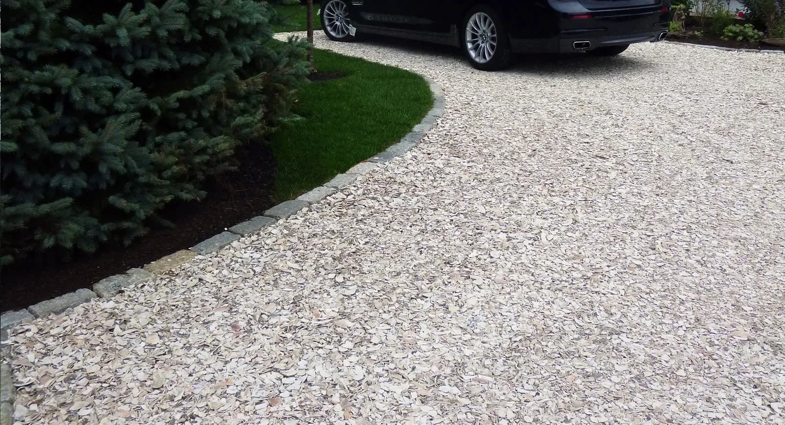 A crushed shell driveway held along a curve by granite cobble edging, with lawn on the other side of it
